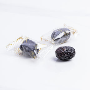 Ajwa Al Madina dates wrapped in a decorative paper, showcasing their dark, glossy appearance and premium quality from Kingdom Dates UAE.